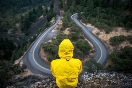 image of person in yellow raincoat sitting up high, looking down at a curvy mountain road