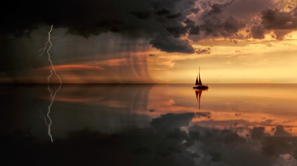 photo of sailboat in a mild rainstorm, during sunset.