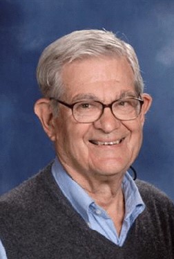 a head-shot of Robert Whitney smiling wearing a light blude oxford shurt and grey pull-over sweater.